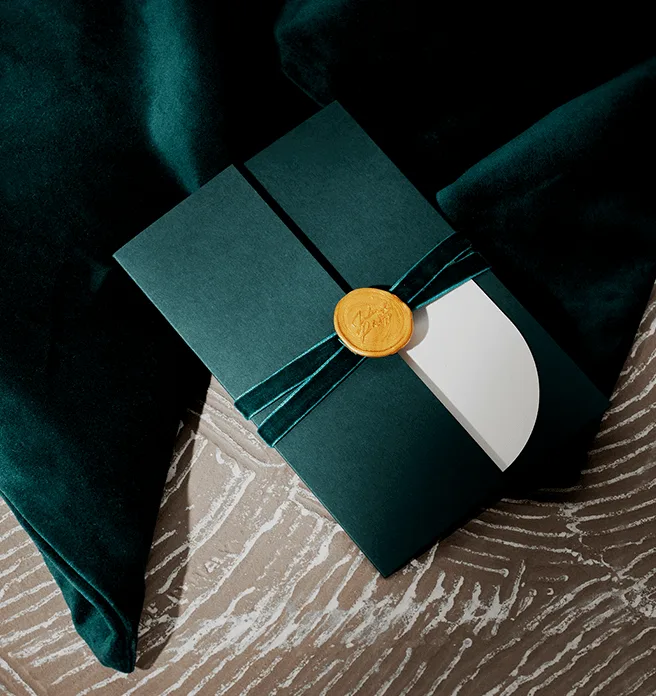 Dunkelgrüne Einladungskarte mit weißer Banderole und goldenem Siegel.
